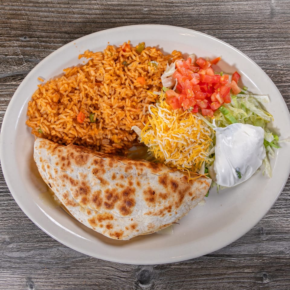 A quesadilla with Mexican rice, shredded lettuce, diced tomatoes, shredded cheese, and sour cream.