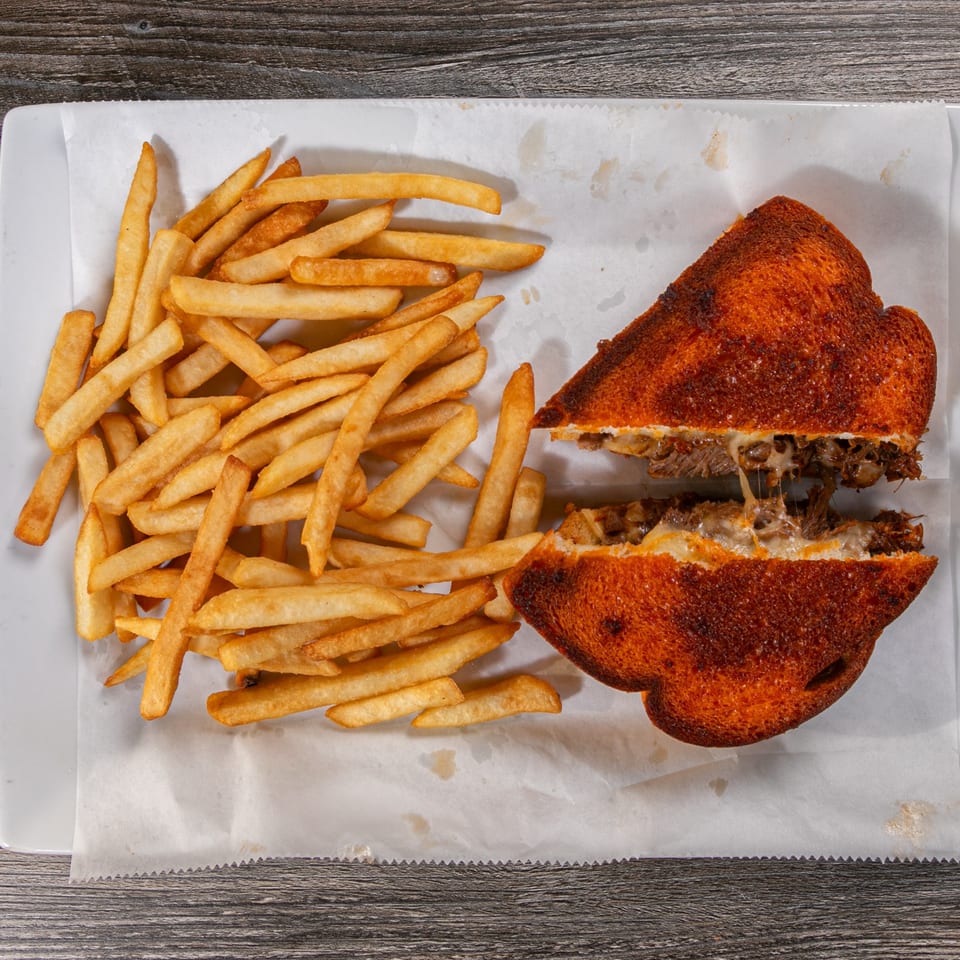 A grilled sandwich, cut in half, with melted cheese and meat, served with a side of fries.