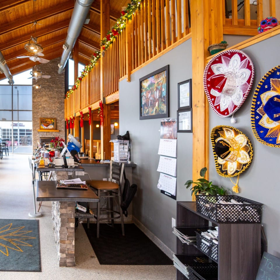 Casa Agave's interior features a high wooden ceiling, festive lights, and colorful sombreros on a gray wall.