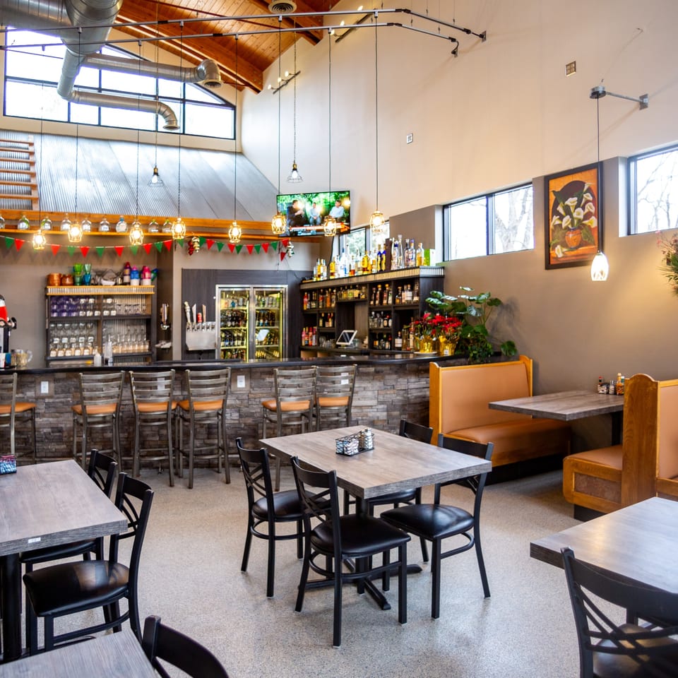 Interior of Casa Agave Mexican Cuisine, featuring a bar with stools, dining tables, and booths.